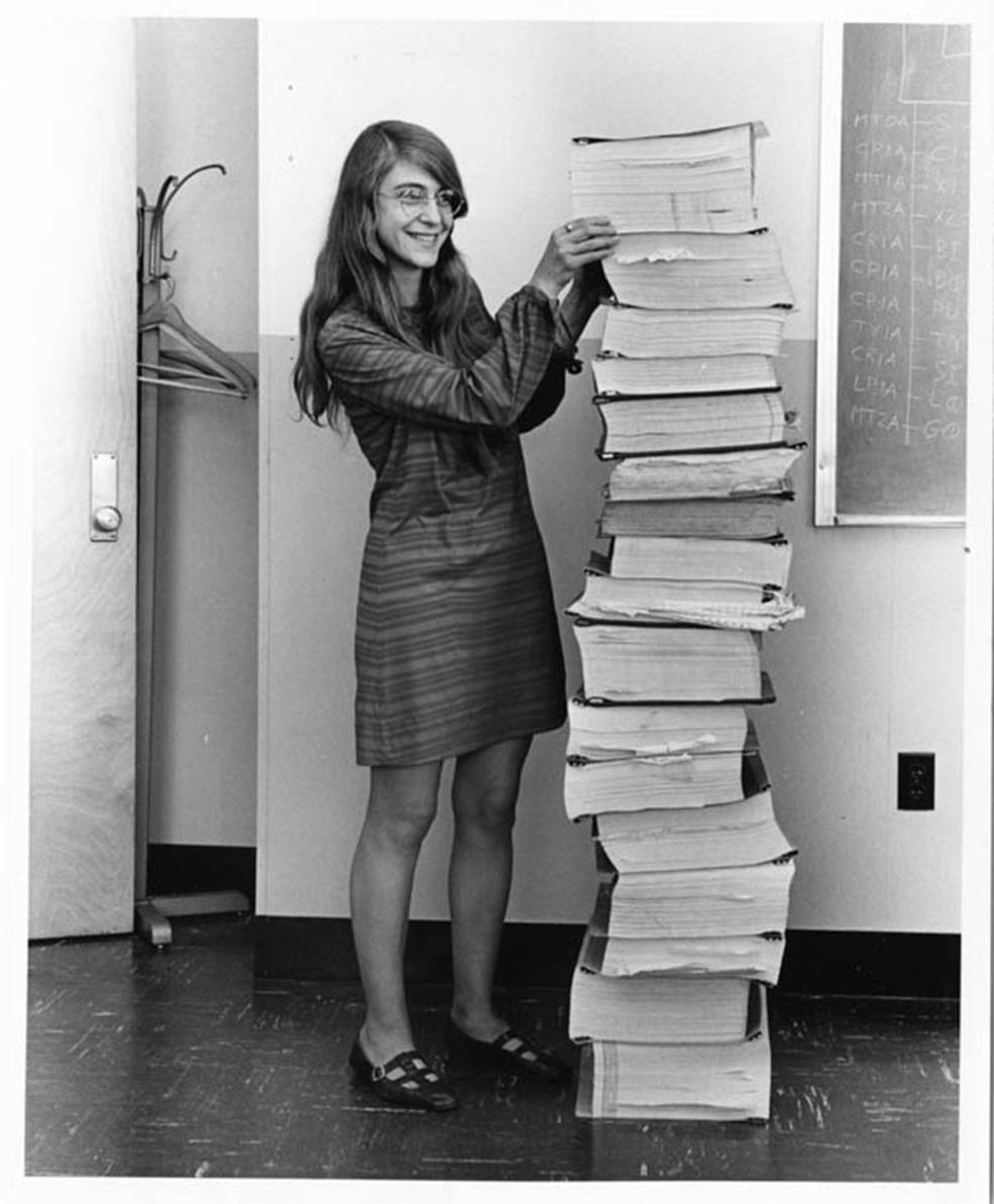 Margaret Hamilton ao lado de uma pilha de códigos-fonte do Apollo Guidance Computer. © Courtesy MIT Museum